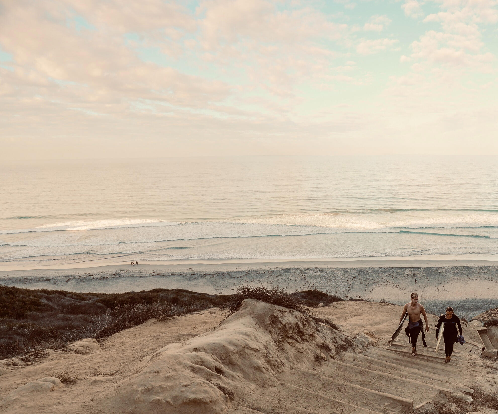 Swell Circle Two surfers walking upstair from the beach with boards, friendly, relaxed energy
